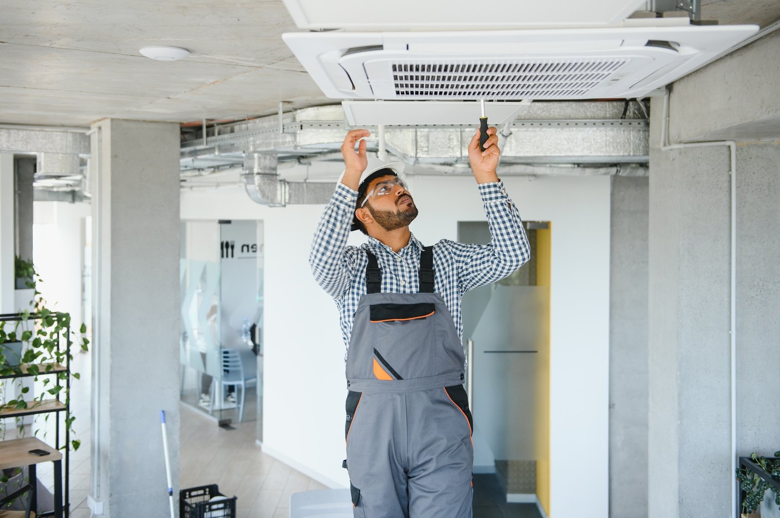 Concentrated young Indian engineer setting up air conditioner